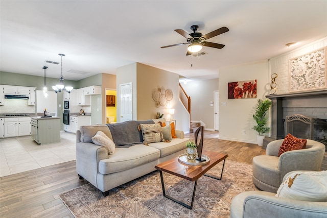 living room with light wood-style floors, a brick fireplace, visible vents, and stairway