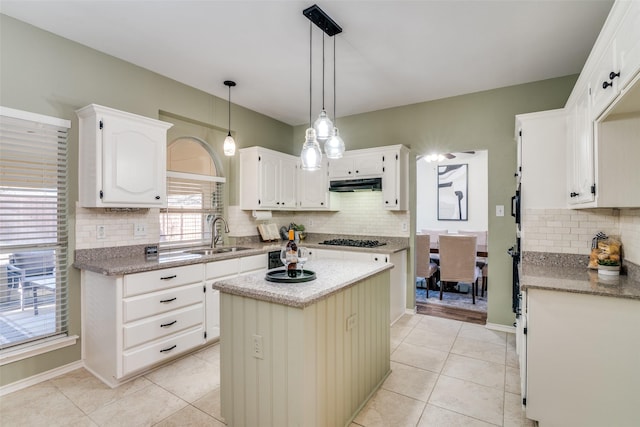 kitchen featuring light tile patterned floors, under cabinet range hood, a sink, white cabinets, and backsplash