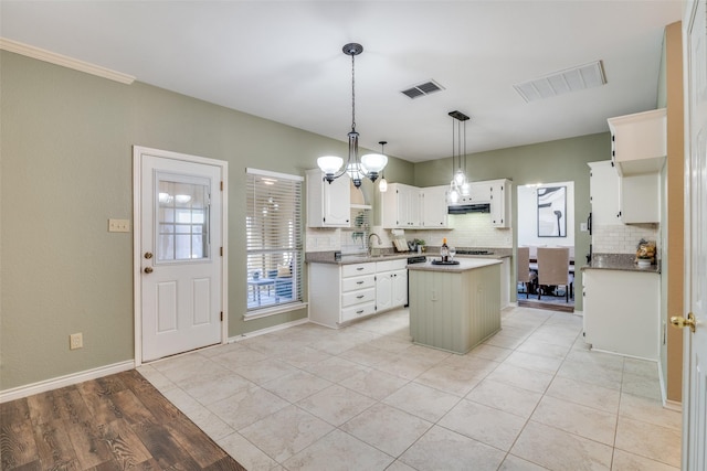 kitchen with visible vents, a kitchen island, under cabinet range hood, and a sink