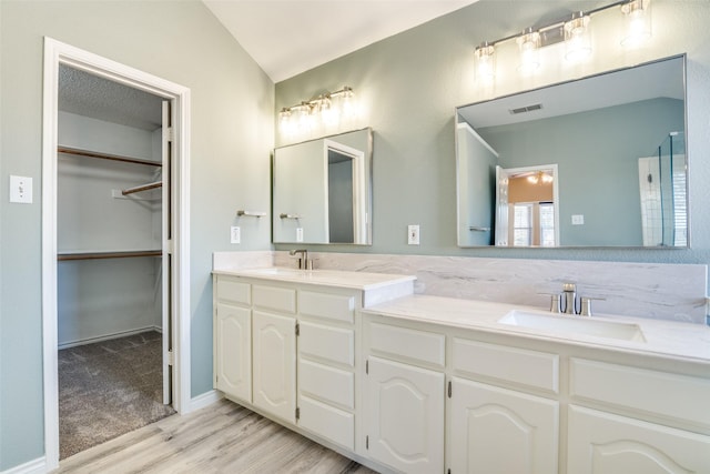 bathroom featuring double vanity, visible vents, a spacious closet, a sink, and wood finished floors