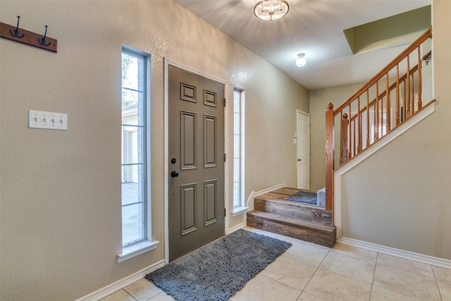 foyer entrance featuring light tile patterned floors, a textured wall, stairs, and baseboards