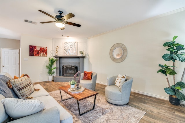 living area with wood finished floors, visible vents, baseboards, ornamental molding, and a brick fireplace