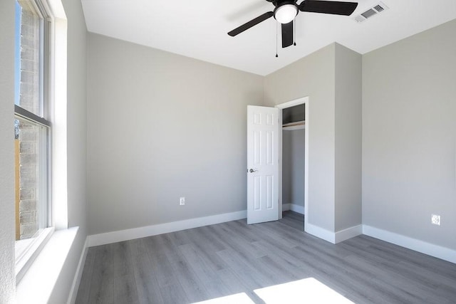 unfurnished bedroom featuring ceiling fan, wood finished floors, visible vents, baseboards, and a closet