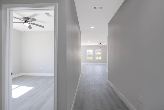 hallway featuring baseboards, visible vents, and wood finished floors