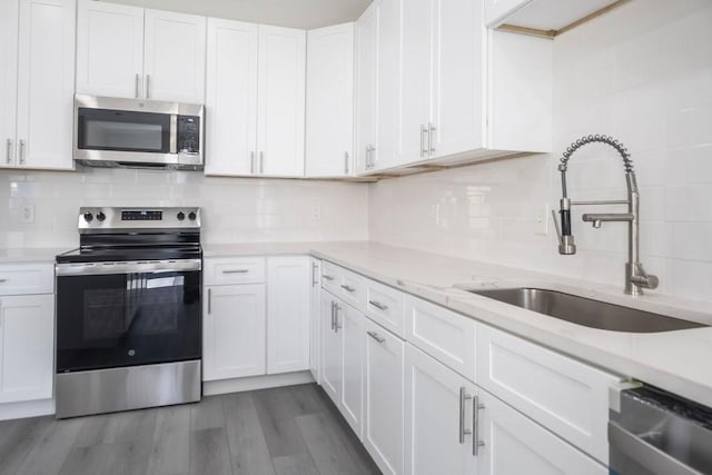 kitchen with stainless steel appliances, wood finished floors, a sink, white cabinetry, and decorative backsplash