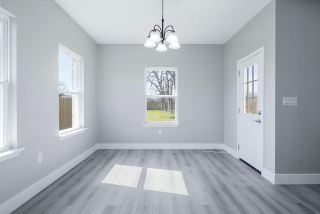 unfurnished dining area featuring an inviting chandelier, baseboards, and wood finished floors