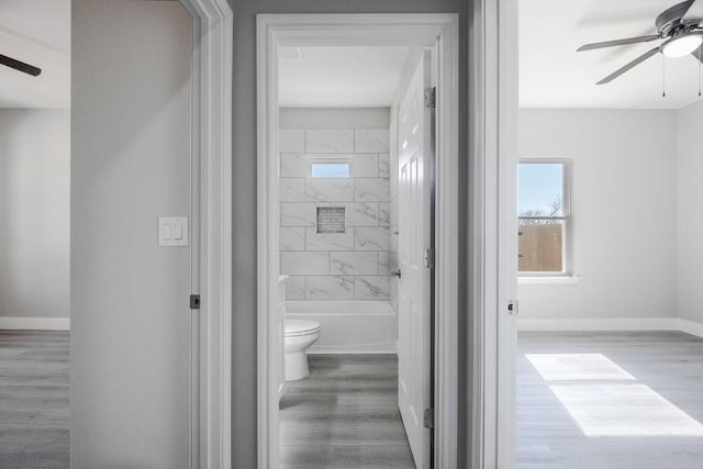 bathroom with baseboards, a ceiling fan, toilet, wood finished floors, and shower / washtub combination