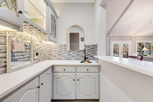 kitchen with light countertops, backsplash, white cabinetry, vaulted ceiling, and a sink