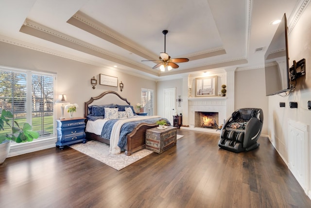 bedroom with dark wood-type flooring, a raised ceiling, and a large fireplace