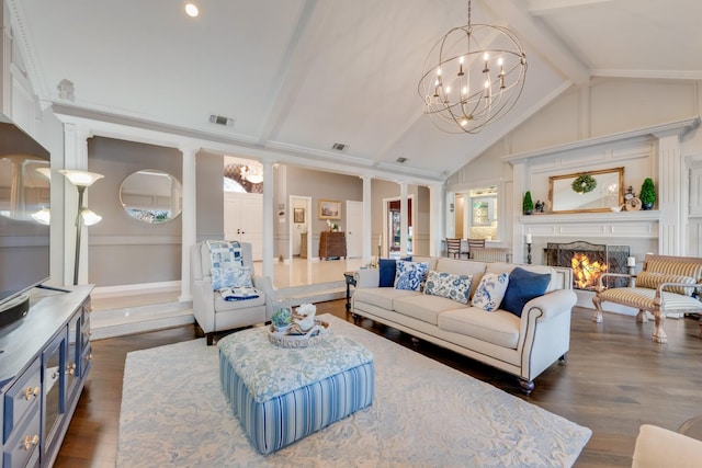 living area featuring a warm lit fireplace, dark wood-style flooring, beam ceiling, ornate columns, and a notable chandelier