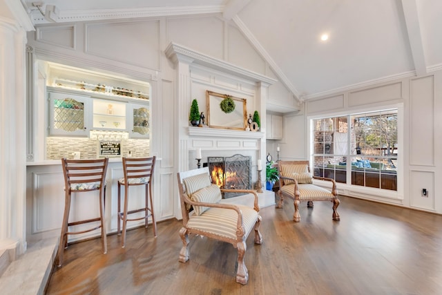 living area featuring a warm lit fireplace, high vaulted ceiling, a decorative wall, wood finished floors, and beamed ceiling