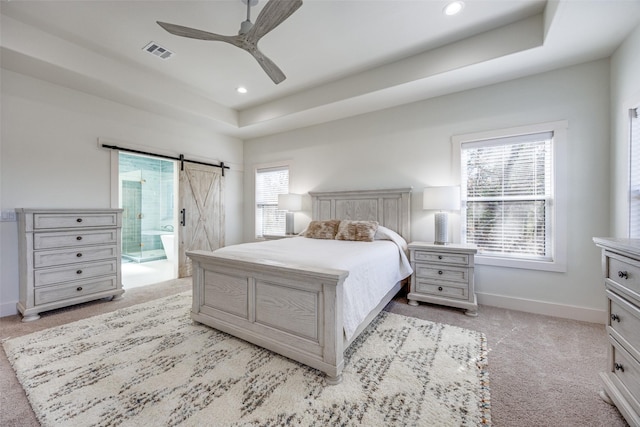 bedroom with a tray ceiling, visible vents, a barn door, light carpet, and baseboards