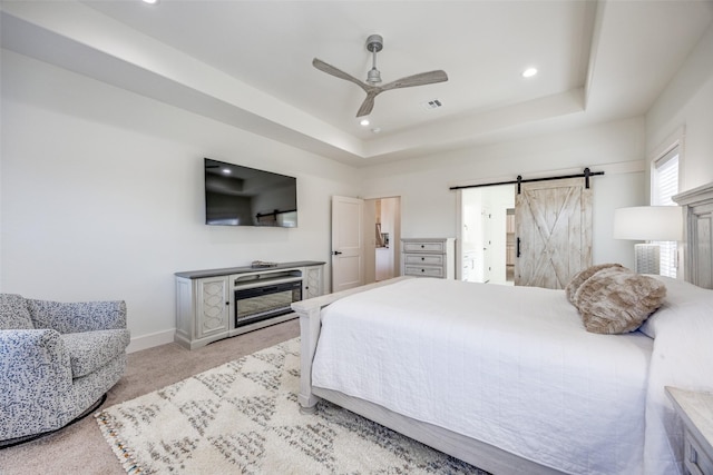 bedroom with a barn door, a tray ceiling, baseboards, and light colored carpet