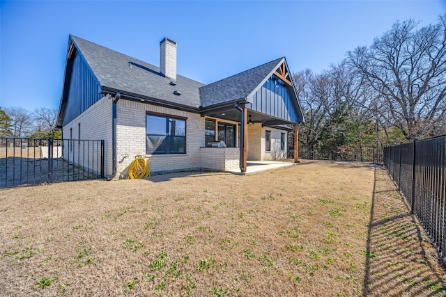 rear view of property with brick siding, a patio, a chimney, a lawn, and a fenced backyard