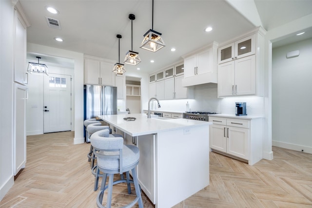 kitchen featuring a sink, visible vents, light countertops, freestanding refrigerator, and an island with sink