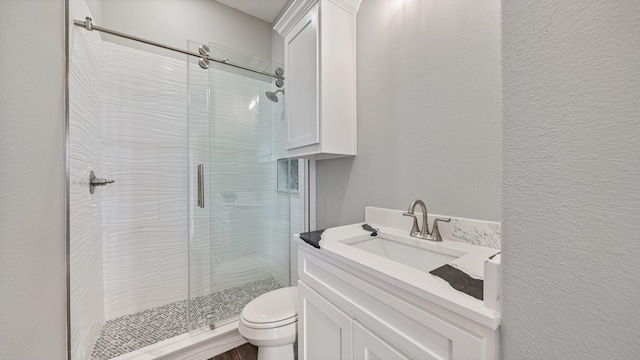 bathroom featuring a textured wall, a stall shower, vanity, and toilet