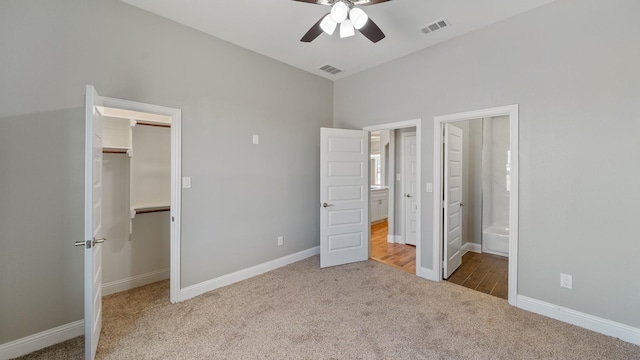 unfurnished bedroom with carpet floors, a walk in closet, visible vents, and baseboards