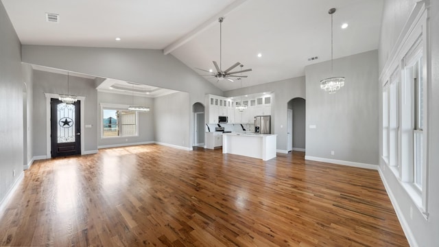 unfurnished living room with visible vents, arched walkways, beamed ceiling, wood finished floors, and ceiling fan with notable chandelier