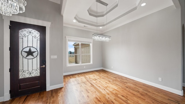 foyer with baseboards, a tray ceiling, wood finished floors, and ornamental molding