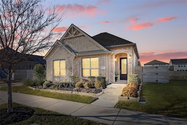 craftsman house featuring roof with shingles, brick siding, a front lawn, and fence