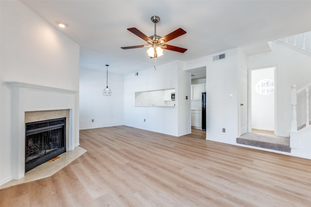 unfurnished living room featuring a high end fireplace, visible vents, stairs, a ceiling fan, and light wood-type flooring