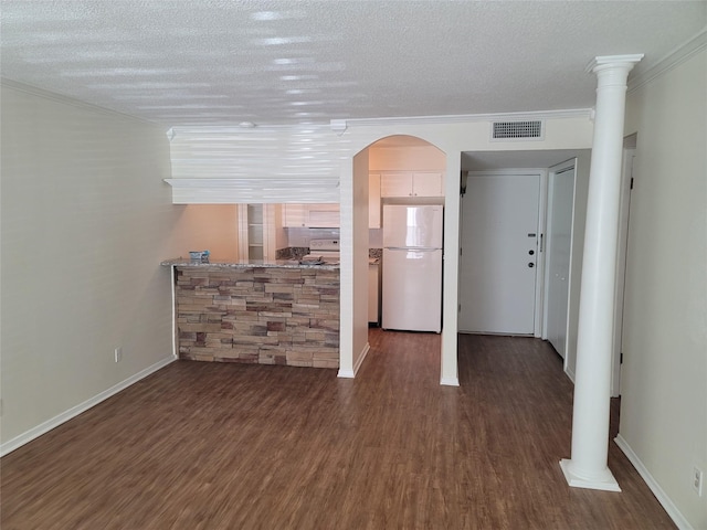 interior space with a textured ceiling, wood finished floors, decorative columns, and visible vents