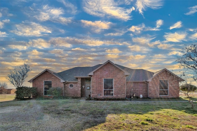 single story home with a shingled roof, a front lawn, and brick siding