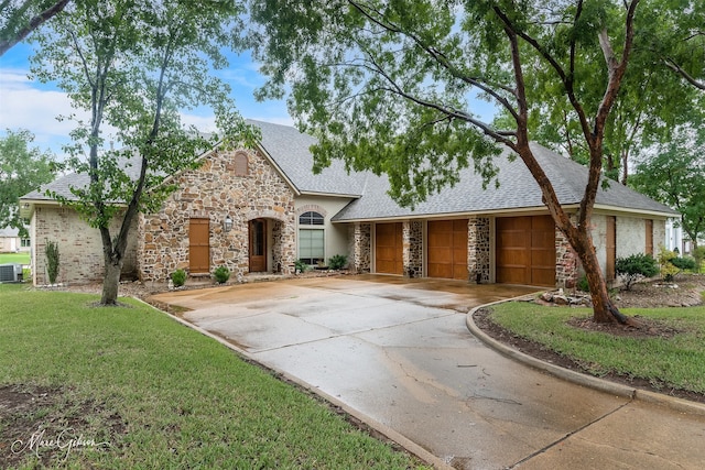 view of front of home with driveway, a garage, stone siding, roof with shingles, and a front yard