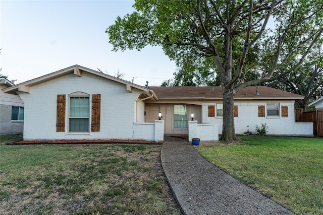 ranch-style house with a front yard, fence, and brick siding