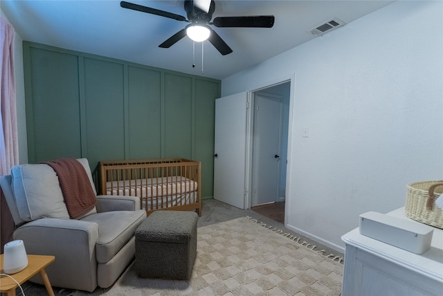 bedroom with a ceiling fan, light colored carpet, visible vents, and a decorative wall