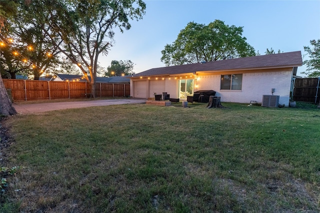 back of house at dusk with brick siding, a patio, a lawn, an attached garage, and a fenced backyard