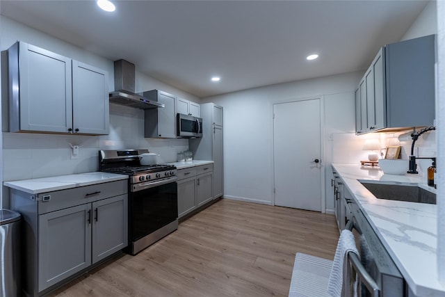 kitchen featuring tasteful backsplash, light wood-style flooring, appliances with stainless steel finishes, a sink, and wall chimney exhaust hood