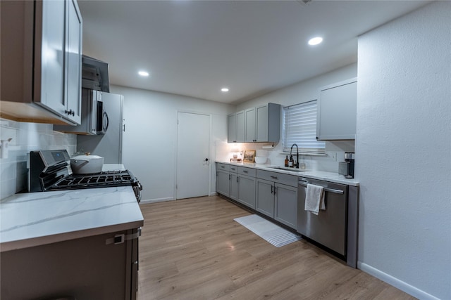 kitchen featuring stainless steel appliances, a sink, gray cabinets, light wood finished floors, and tasteful backsplash