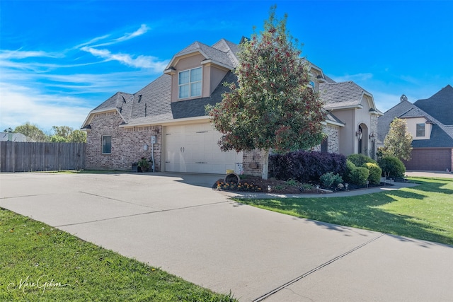 french country style house with brick siding, an attached garage, a front yard, fence, and driveway