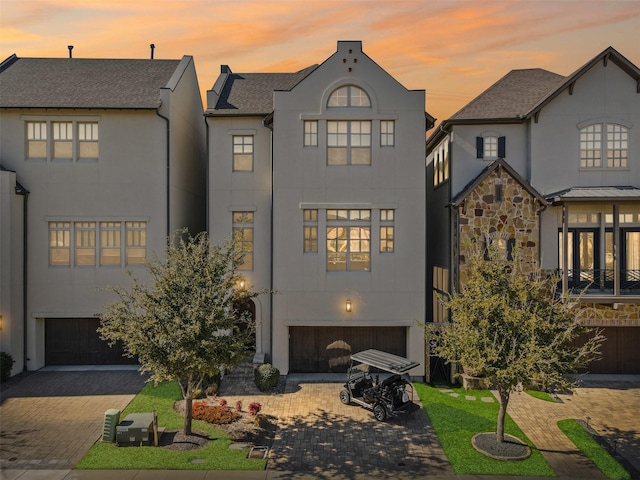 rear view of house with stone siding, decorative driveway, an attached garage, and stucco siding