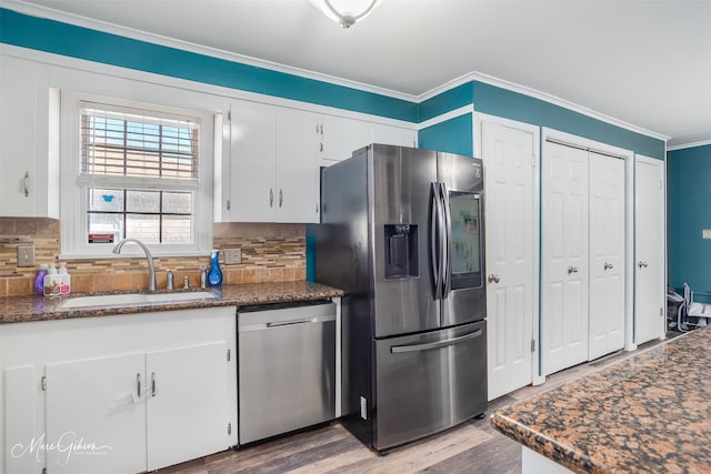 kitchen featuring decorative backsplash, appliances with stainless steel finishes, ornamental molding, white cabinetry, and a sink