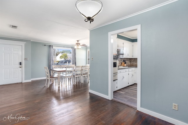 dining room featuring dark wood-type flooring, a ceiling fan, baseboards, visible vents, and crown molding