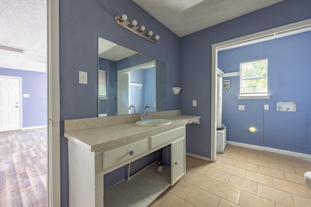 full bath with a textured ceiling, vanity, visible vents, baseboards, and tile patterned floors