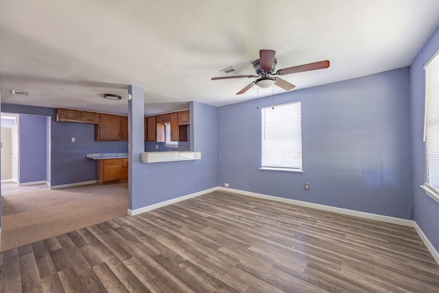 unfurnished living room with ceiling fan, visible vents, baseboards, and wood finished floors