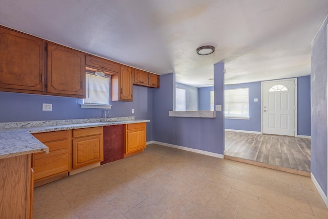 kitchen featuring light stone countertops, baseboards, brown cabinetry, and a sink