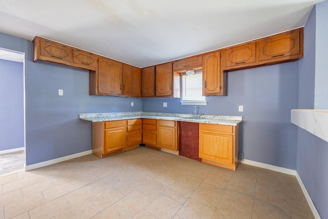 kitchen with brown cabinetry, a sink, light stone countertops, and baseboards