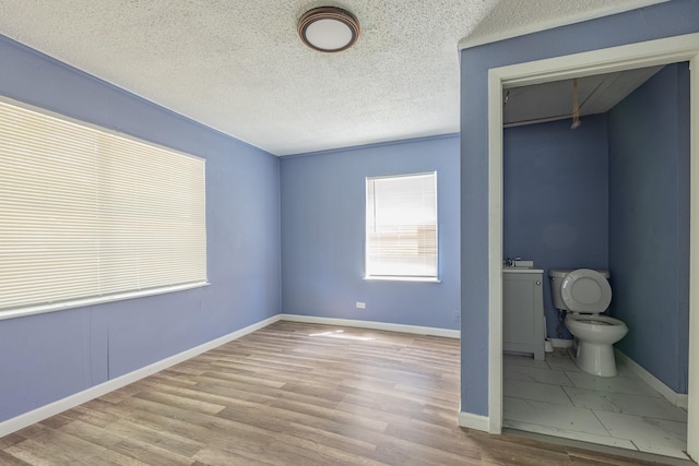 unfurnished bedroom featuring attic access, baseboards, wood finished floors, a textured ceiling, and a sink