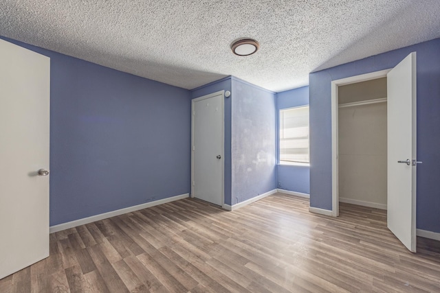 unfurnished bedroom featuring a closet, a textured ceiling, baseboards, and wood finished floors