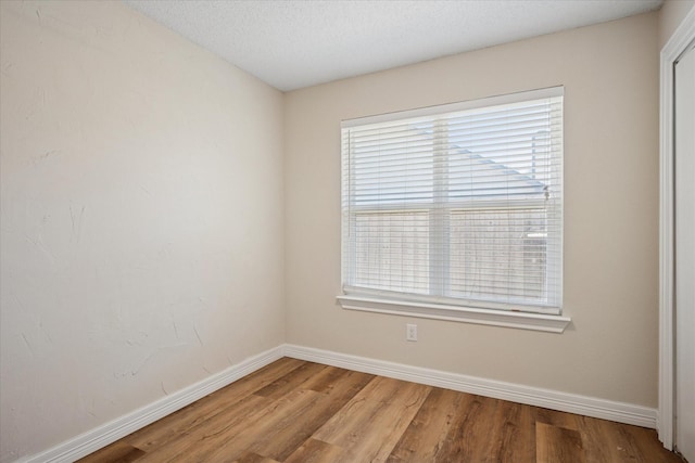 empty room with a textured ceiling, wood finished floors, and baseboards