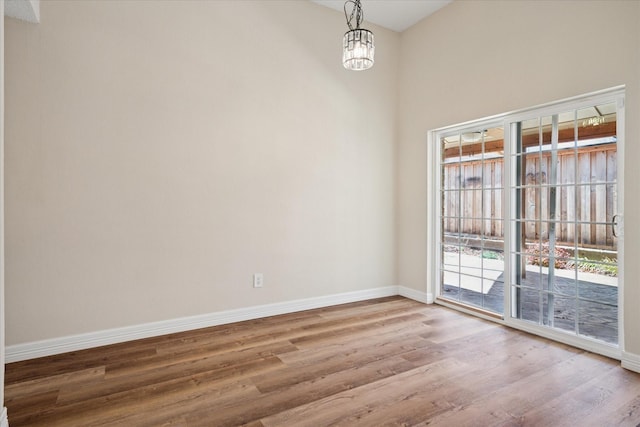 spare room featuring a notable chandelier, baseboards, and wood finished floors