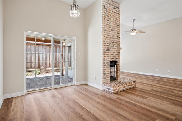 unfurnished living room with a brick fireplace, a high ceiling, baseboards, and wood finished floors