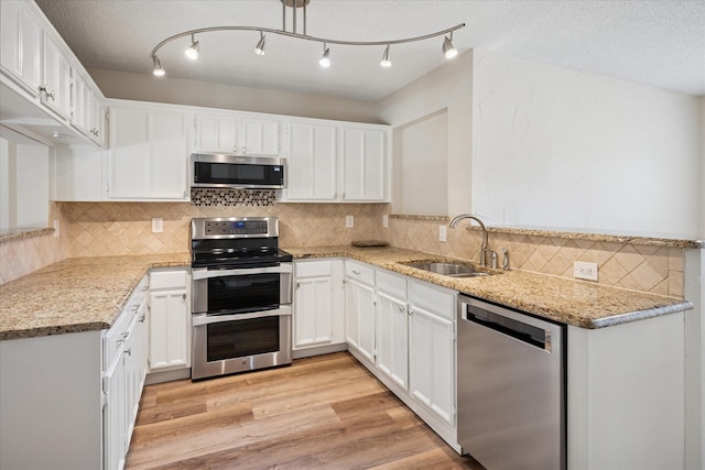 kitchen featuring light wood finished floors, white cabinets, light stone countertops, stainless steel appliances, and a sink