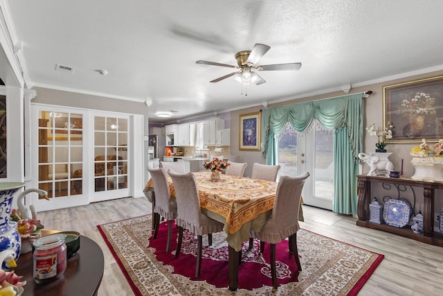 dining space featuring french doors, light wood-type flooring, visible vents, and crown molding