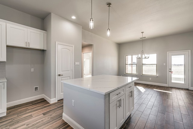 kitchen with light stone counters, a center island, dark wood finished floors, white cabinets, and baseboards