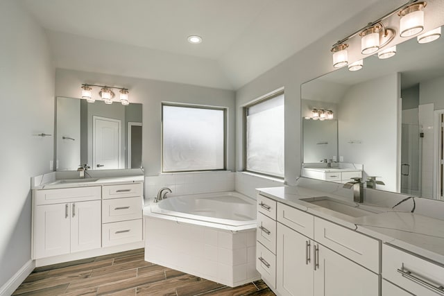 bathroom with a garden tub, wood finished floors, two vanities, and a sink